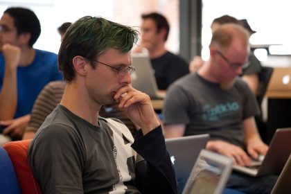 A programmer reviewing lines of code on a large monitor in a dim office.