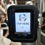 A contactless fare reader on a train invites passengers to tap here and pay, the everyday face of digital payments.