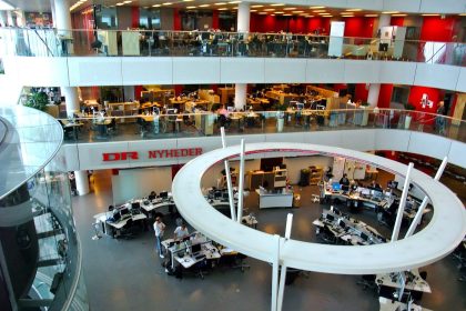 Photograph of journalists working at screens in a busy newsroom checking information.