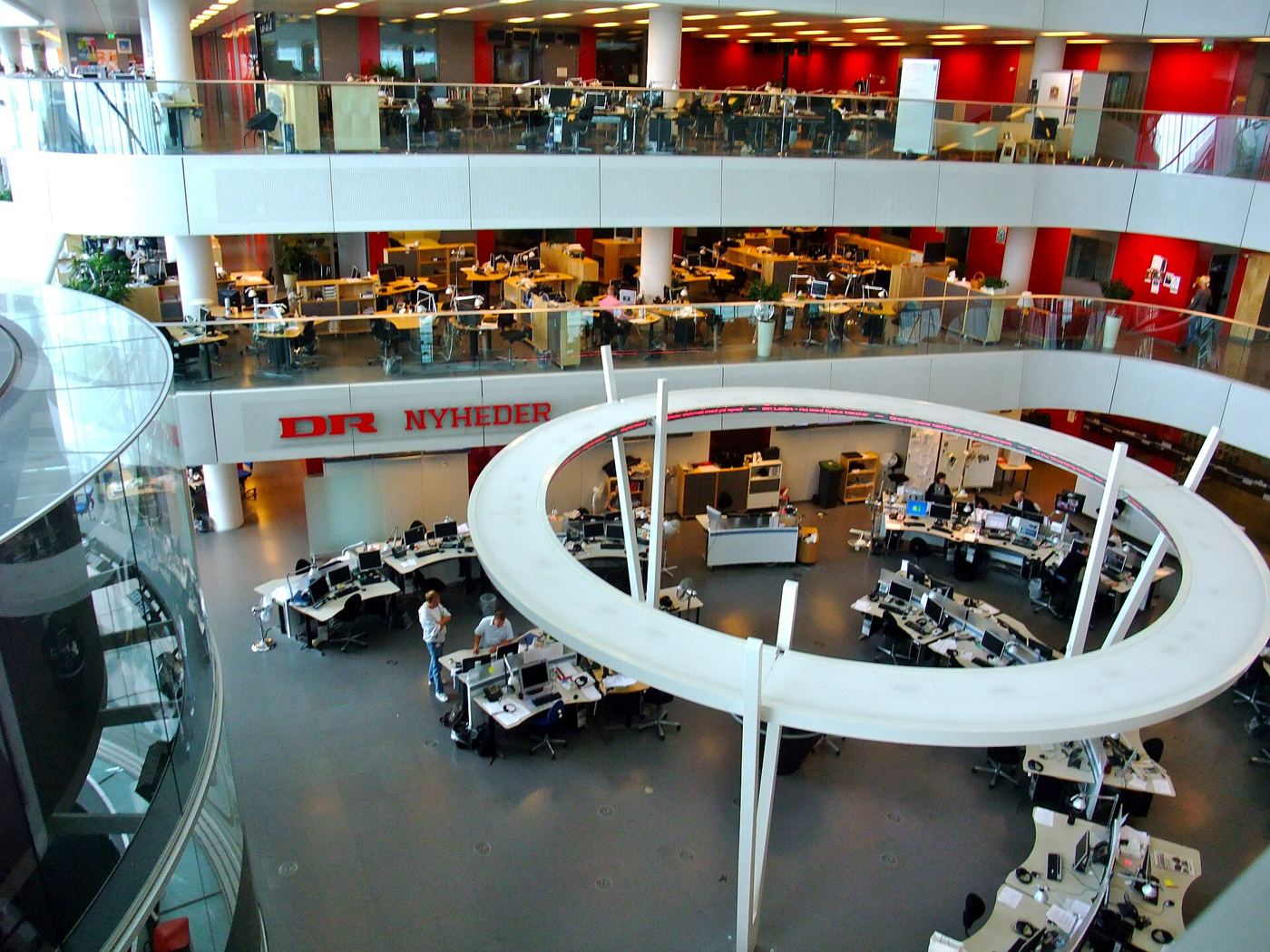 Photograph of journalists working at screens in a busy newsroom checking information.