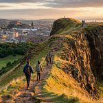 Arthur's Seat hill overlooking Edinburgh at golden hour with hikers on the summit path